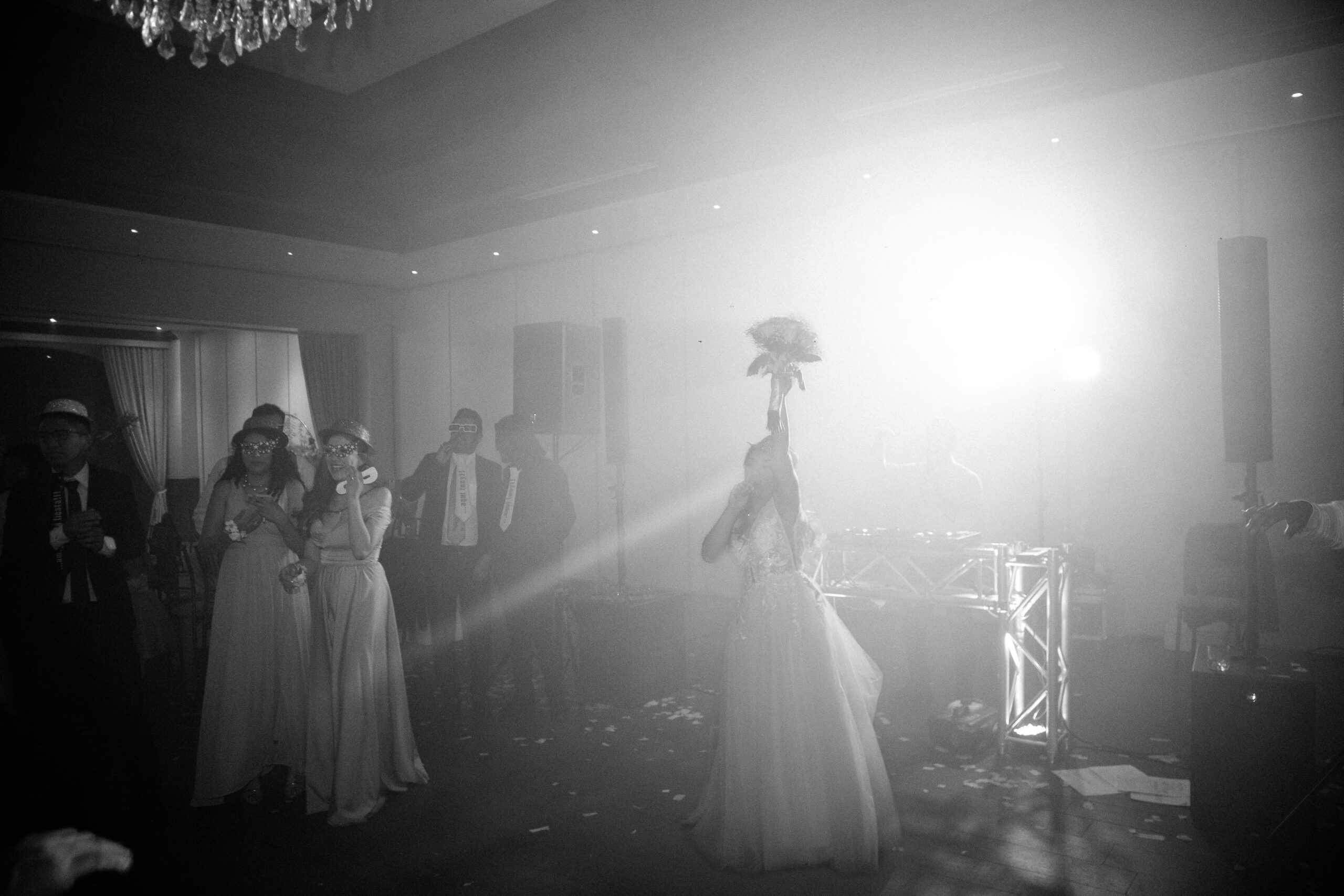 Bride tossing bouquet in vibrant wedding reception. Black and white, joyful, candid moment.